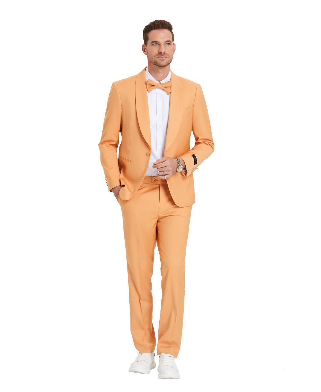 A model wearing a Light Orange prom tuxedo from KCT Menswear, featuring a slim-fit design with a single-button closure and shawl lapel. The tuxedo comes with a matching bowtie for a coordinated and polished look. Perfect for proms and other formal events